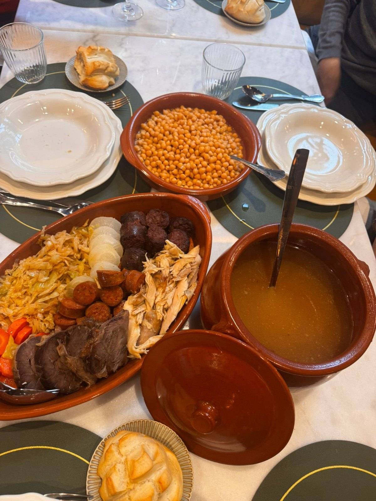 Mesa con cocido madrileño en cazuelas de barro, garbanzos y caldo