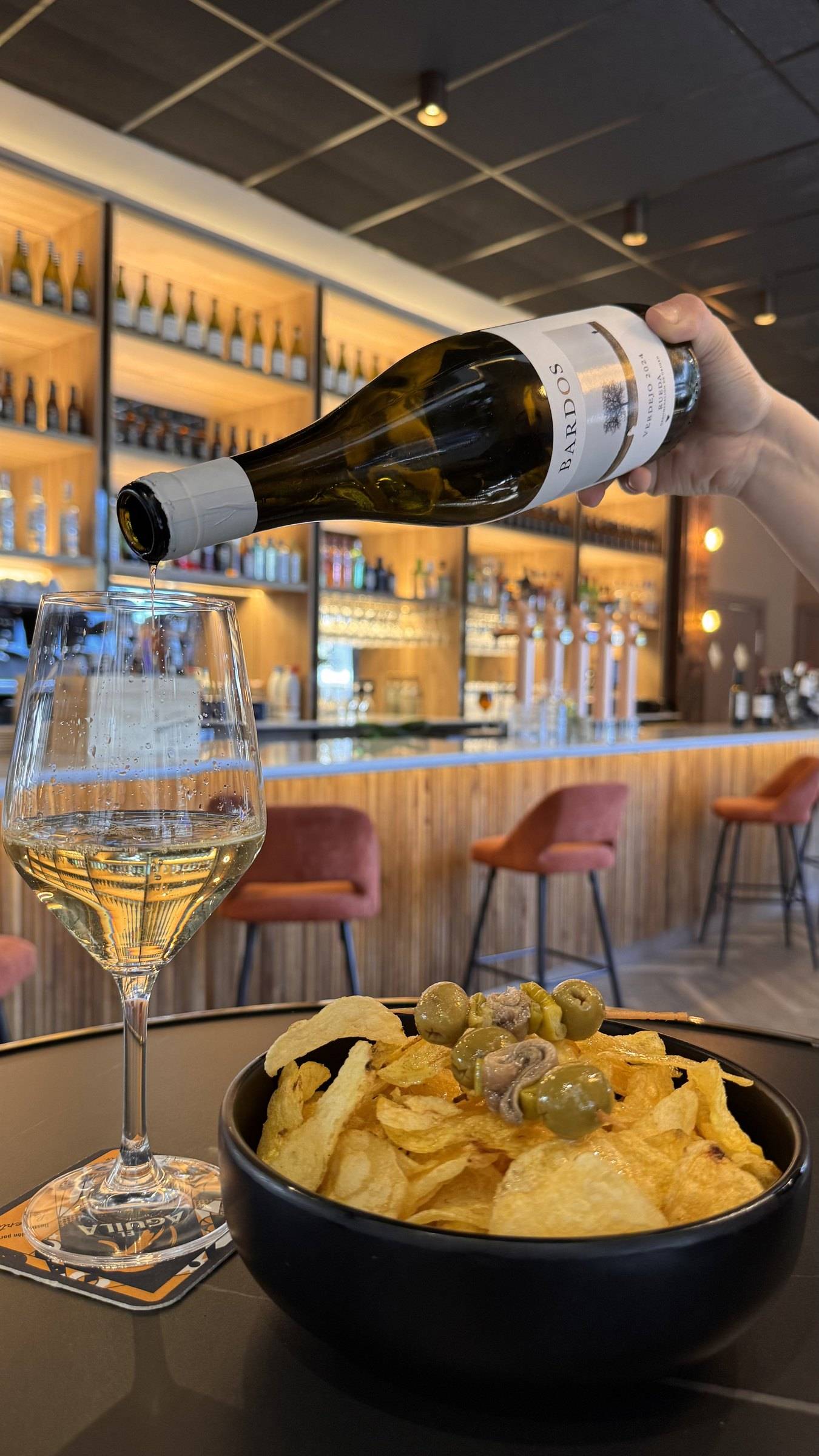 Copa de verdejo servida en la barra junto a un cuenco de patatas con gilda